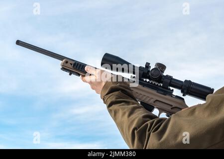 A sniper rifles aim from a rifle with an optical sight in man`s hands sunny blue sky Stock Photo